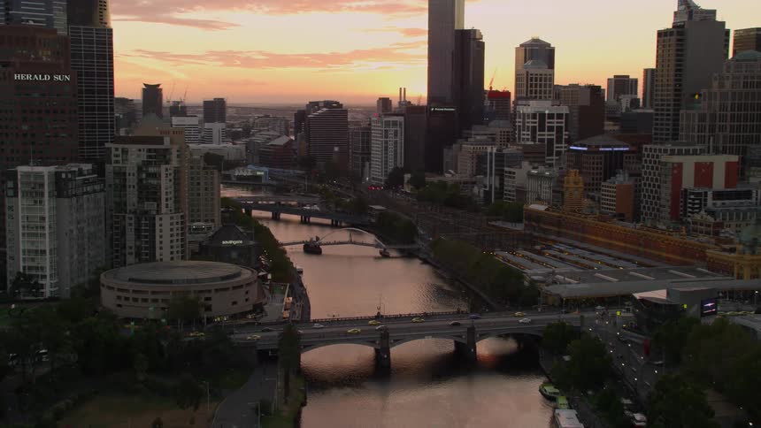 River cuts through city downtown under red sky with sun on horizon