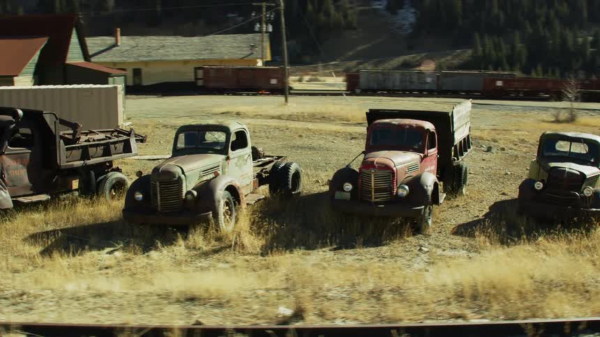 A row of antique broken down vehicles sit on the side of the train tracks