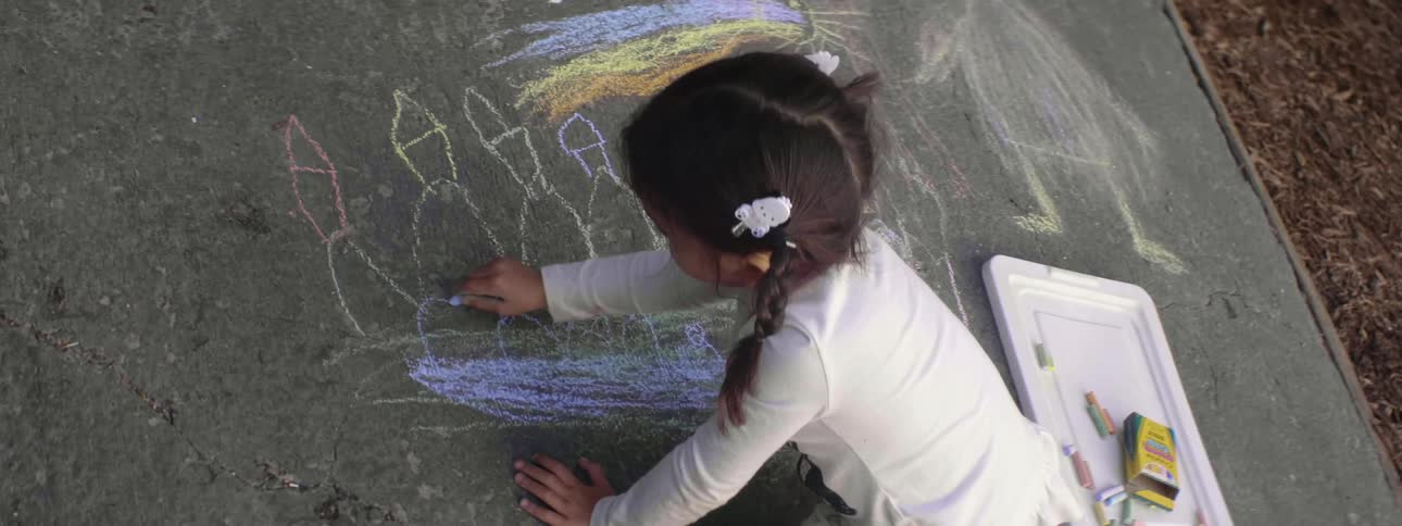 A young girls colors on cement with sidewalk chalk