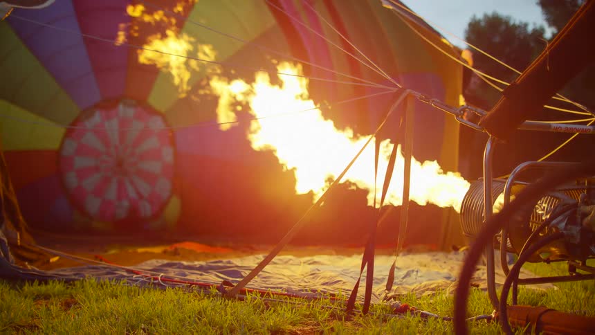 A man holds the side of the hot air balloon as the flame fills it with hot air