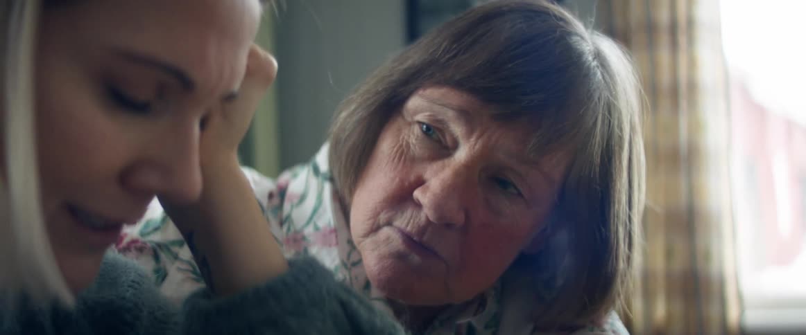 An elderly woman comforts a crying young woman while in home during the daytime