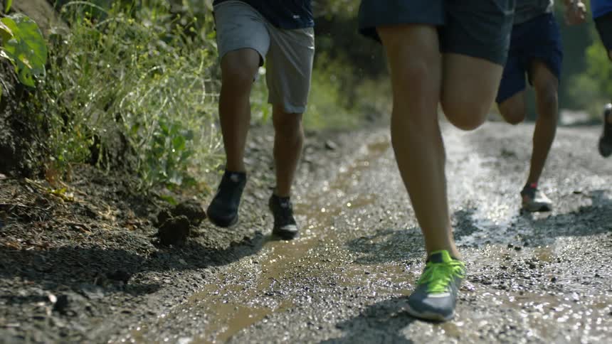 People with sneakers running on a wet dirt road with water and mud