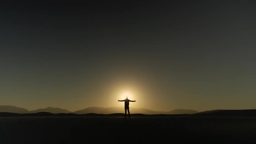 Man raising his hands is silhouetted against the sun in the field