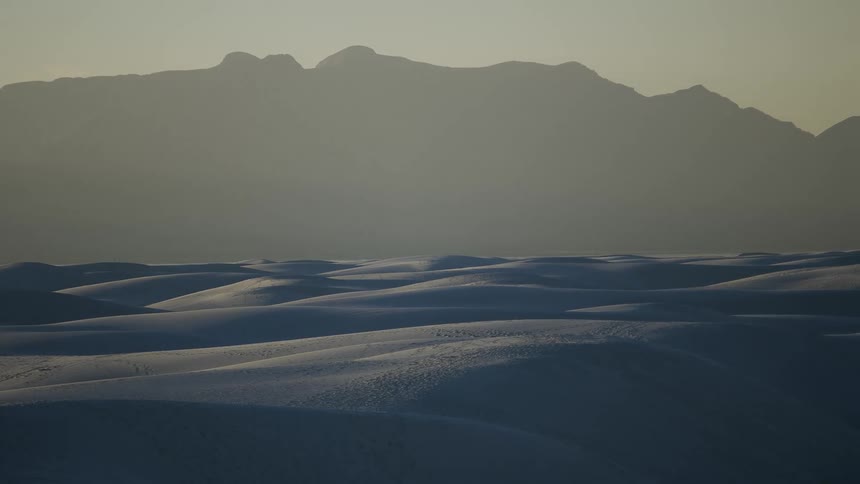 Snow covered hills in front of a mountain range at sunset