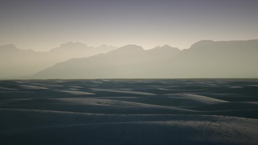 The mountains past the desert are covered in fog