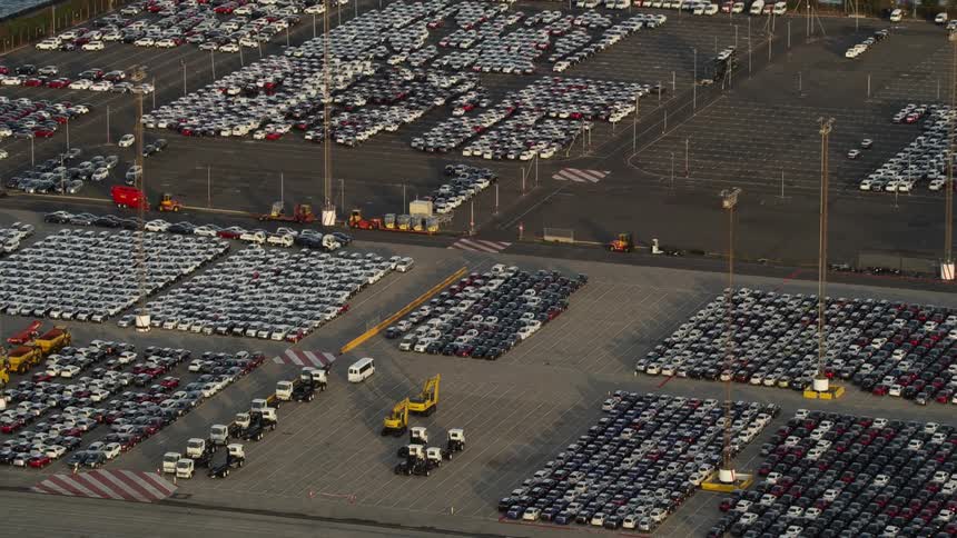 A huge parking lot near the ocean is full of cars and trucks and utility vehicles