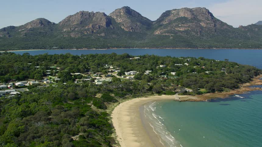 Houses surrounded by trees near the beach with a mountain range the sky and clouds in the background