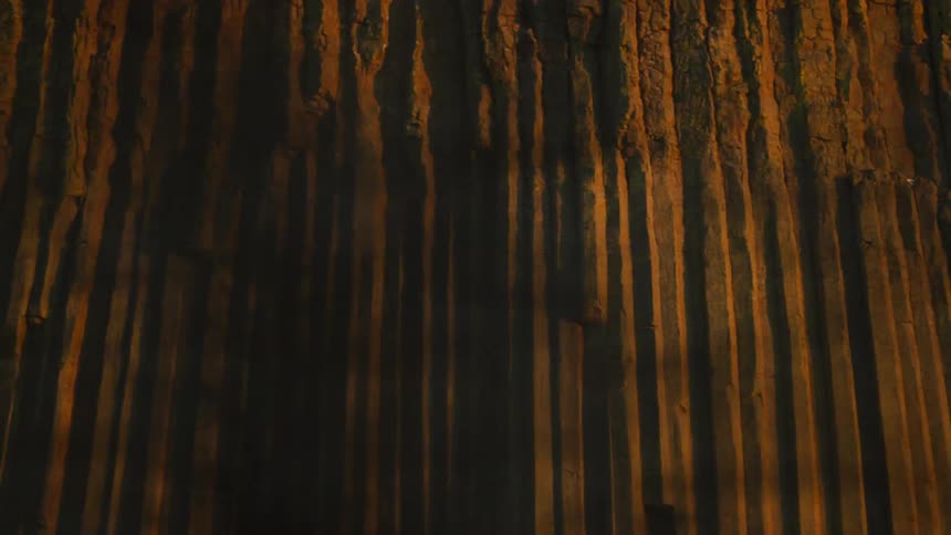 Passing by a huge rocky cliff wall in the distance as seen through the trees while passing by at sunset