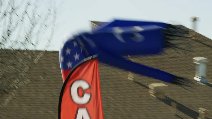 A car dealership with an inflatable tube man waving in the wind with buildings the sky and clouds in the background