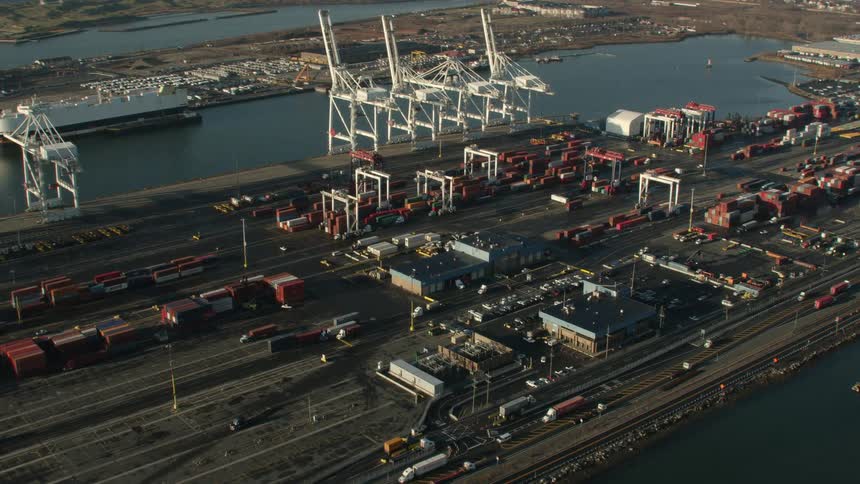 Trucks travel in a shipping yard on the waterfront with shipping cranes idle
