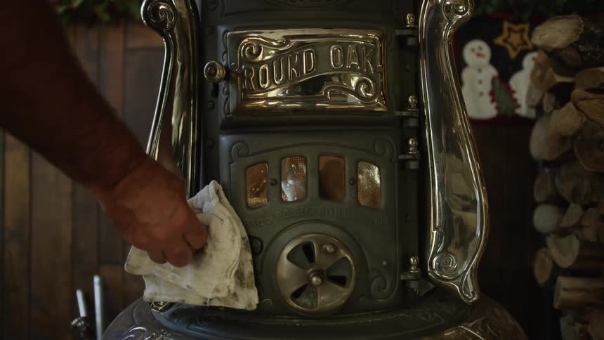 Man closes the door of a vintage iron cabin cook stove with wood burning inside
