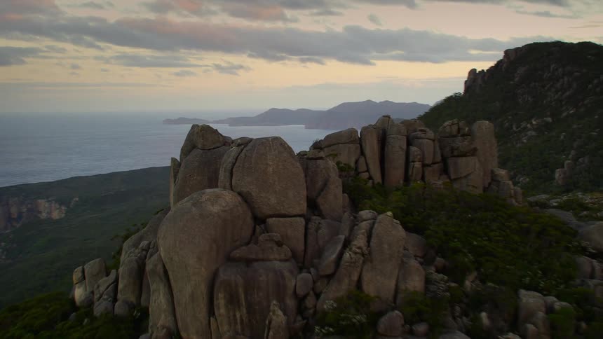 Tall rocks stand on the top of a peak near the coast