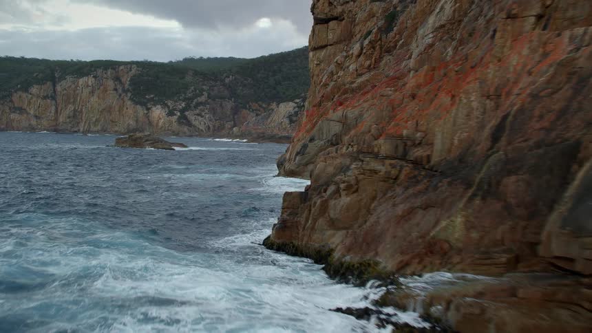 A rocky shore with waves and water with the sky and clouds in the background
