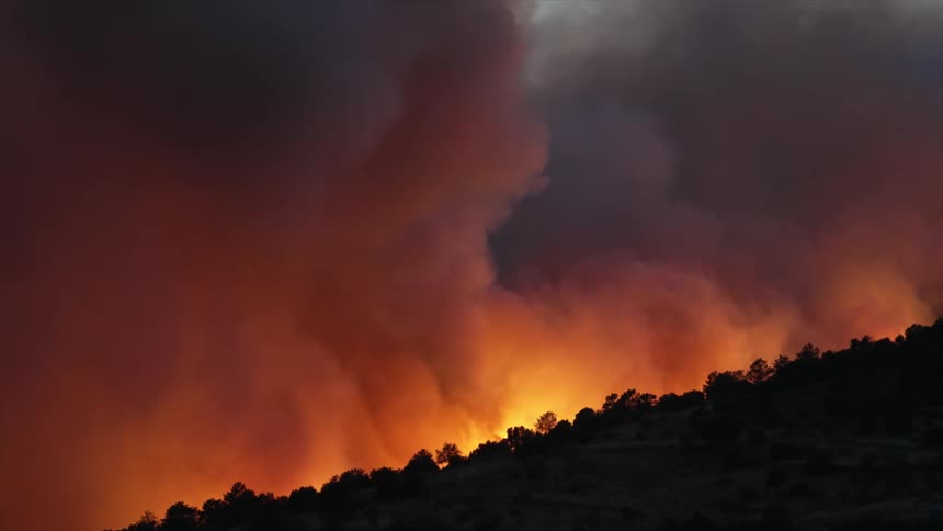 Red flames of a forest wildfire in the mountains reflecting in the clouds of smoke