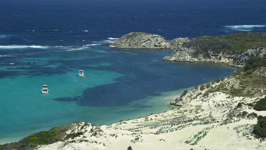 Two boats sail off the coast of an isolated beach