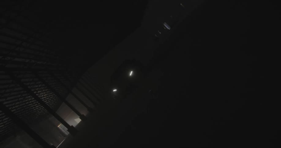 A car with the headlights on is traveling through a dark parking garage