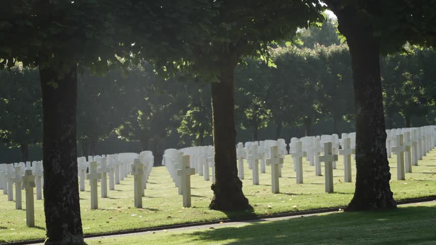 A cemetery with trees grass a pathway and white crosses