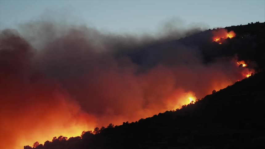 Fire burns the trees on the side of a large hill