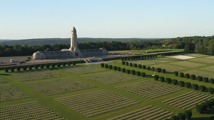 A cemetery with grass and hedges with trees the sky and clouds in the background