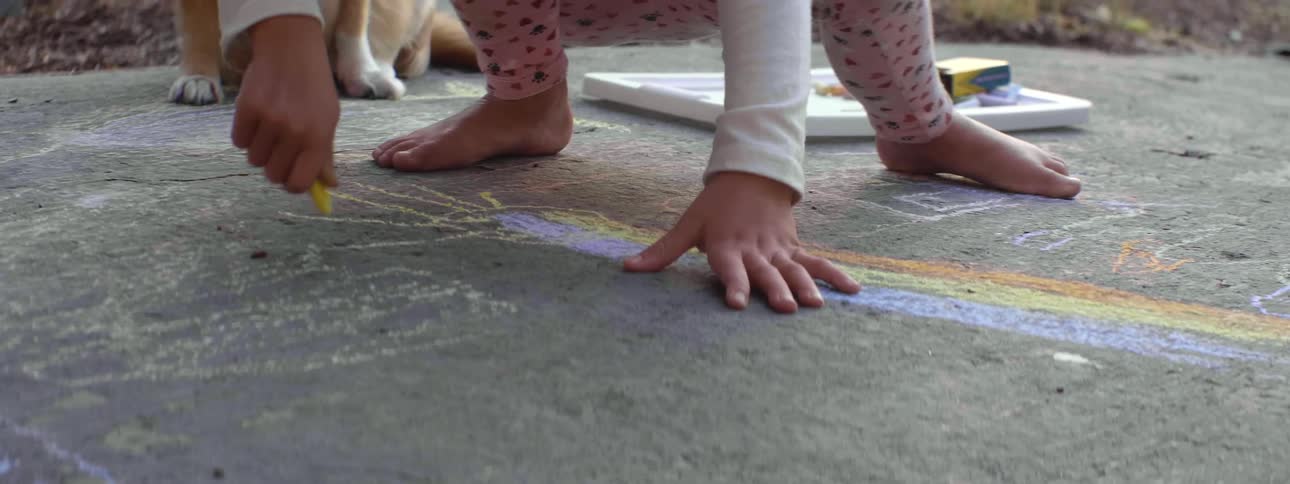A child drawing on the floor with colored chalk outdoors