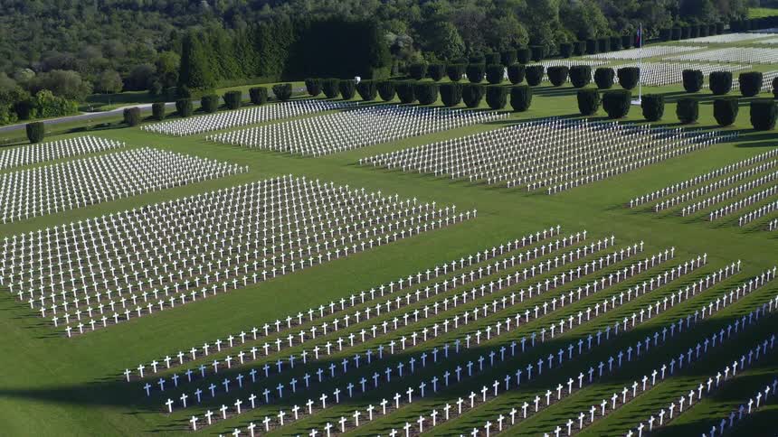 Rows of white crosses in a military cemetery with green grass and landscaped hedges