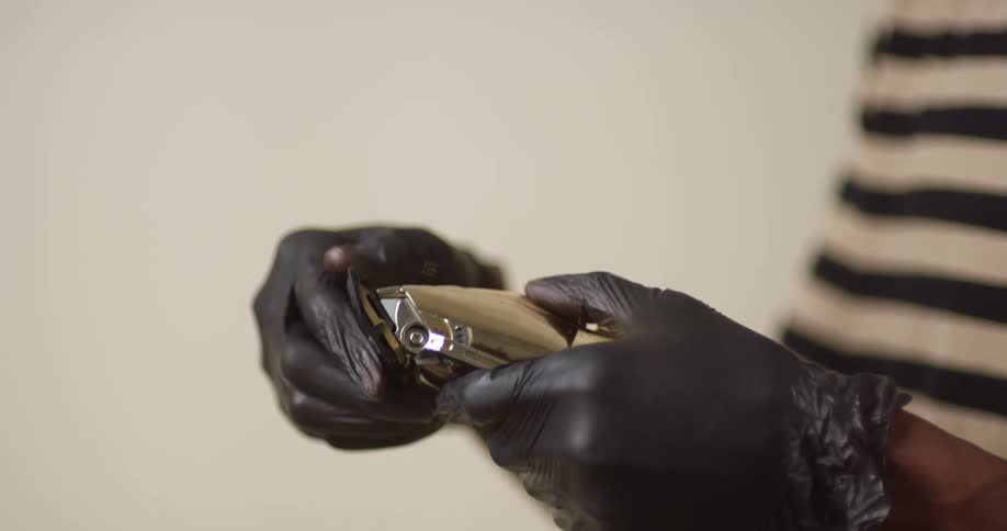 The gloved hands of a young, black barber putting the cap back on an electric hair-trimmer/razor.