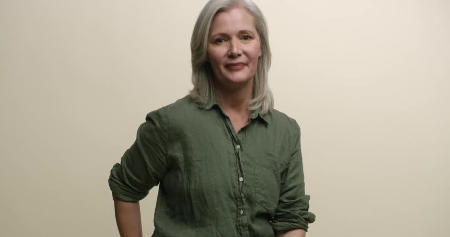 A mature Caucasian female model with gray hair and aged faced smiles at the camera with closed lips