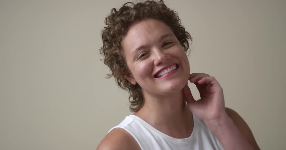 A young, happy freckled woman with short curly hair gives a big dimpled smile to the camera as she changes poses.
