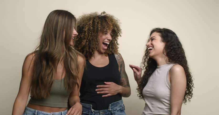 Three young and diverse female friends standing together, laughing, and smiling in a happy moment.