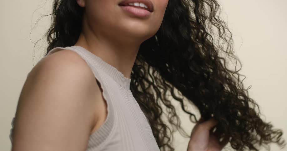 A young, ethnic woman with a relaxed smile runs her hands through her thick, dark, curly hair.