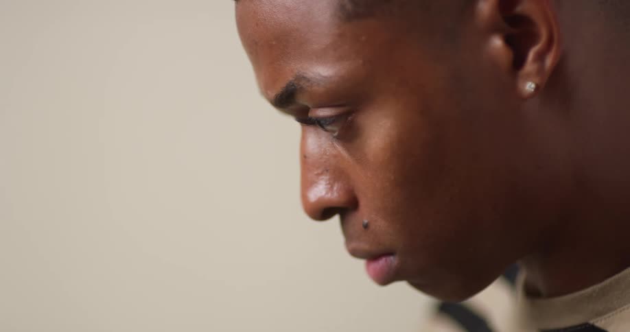 A young, black man is looking down and concentrating while deep in thought.