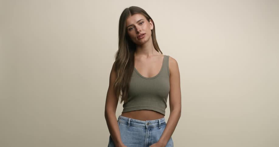 A white female adolescent model wearing a crop top pushes her hair back on one side as she poses