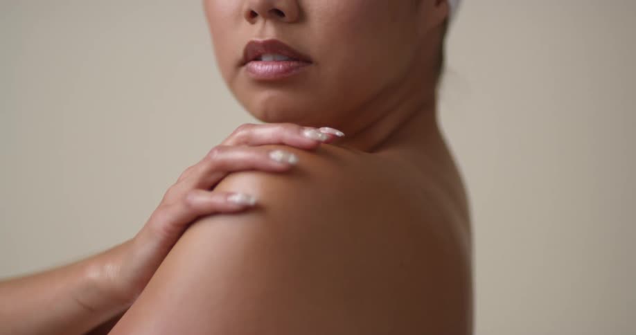 A woman wearing only a towel rubs her manicured hand up her arm to her shoulder and back down again.