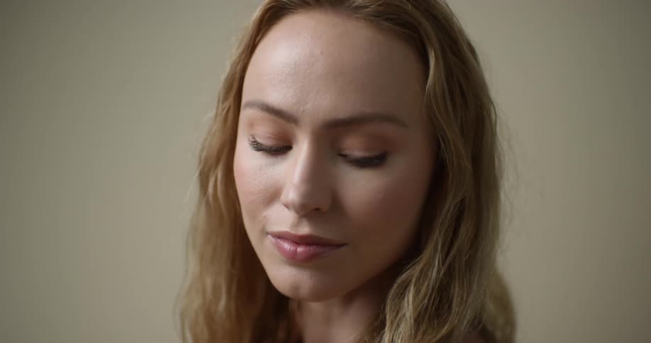 Close up of a young, blonde Caucasian woman with light eyes, a cleft chin, and full lips as she looks up, then down and to the side, tucking her chin.