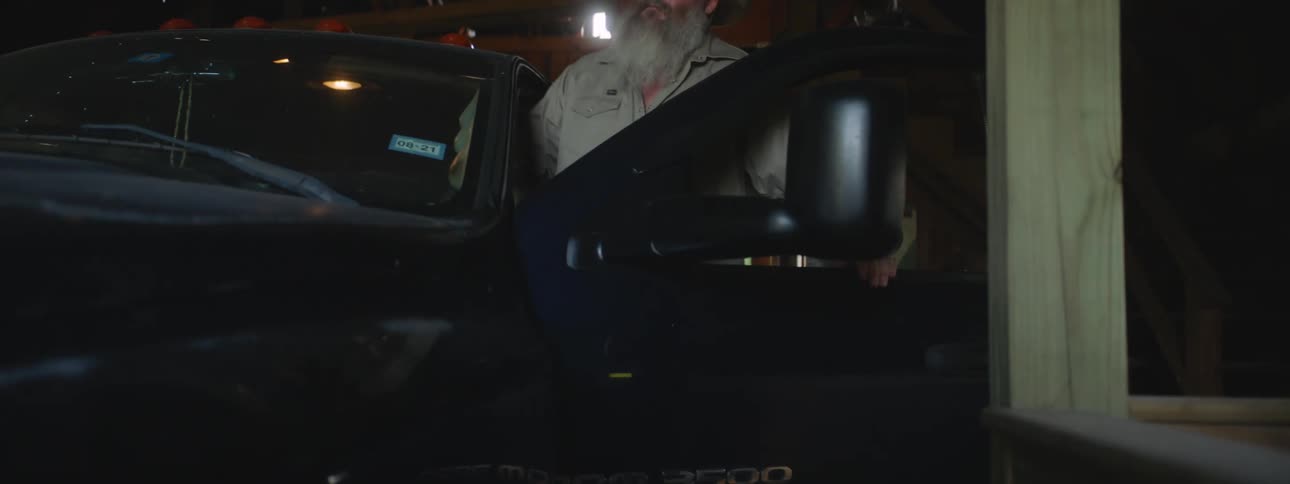 Mature bearded man boarding a black truck parked inside a barn