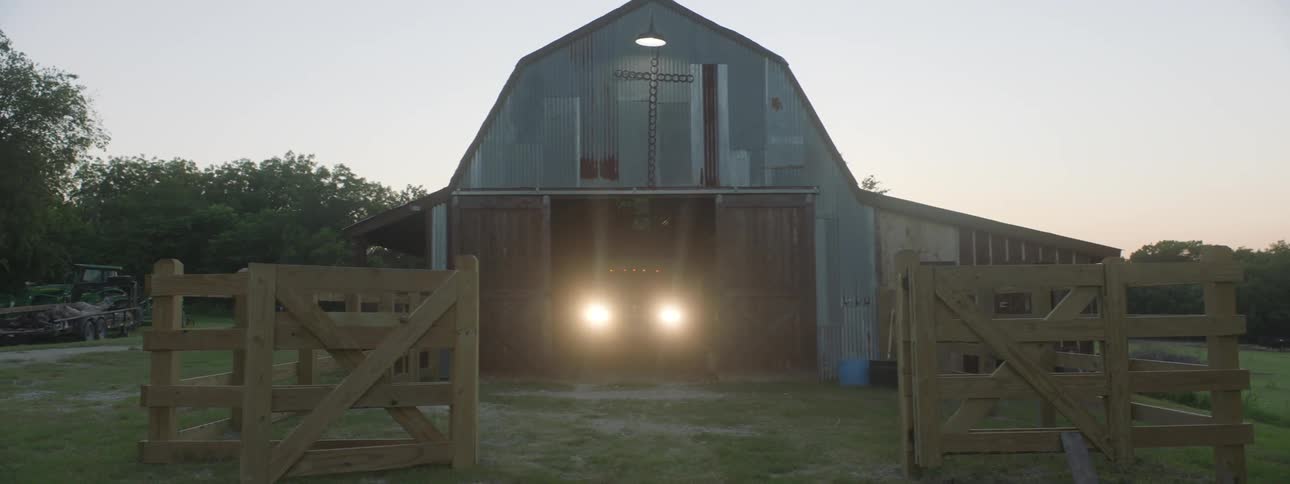 A truck parked inside a barn turns on the headlights and drives out