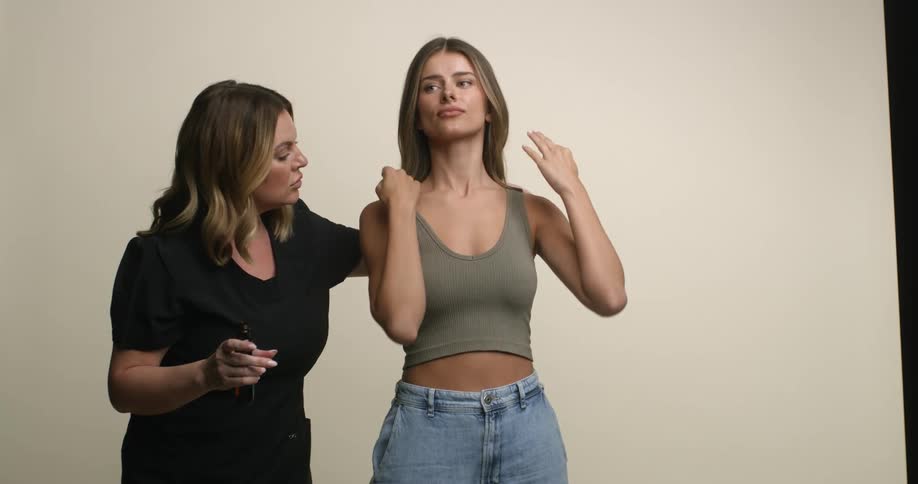 Female photography assistant adjusting a young, white, female model's tank top for a photo shoot