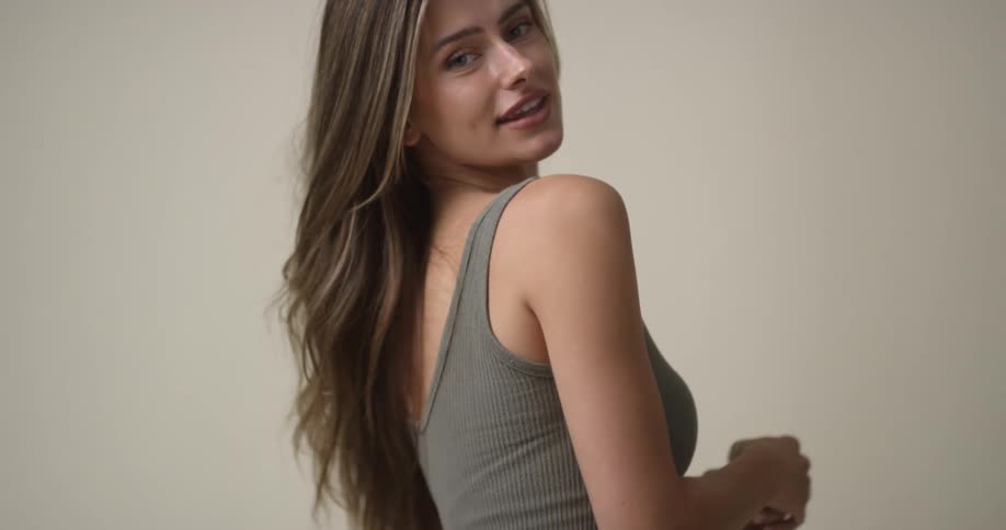 A young, Caucasian woman tosses her hair back and forth as she gives a sultry smile, poses, and does a turn.