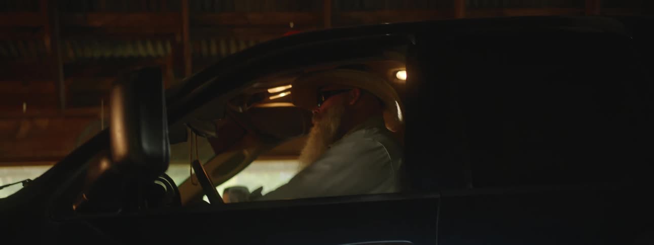 A man with a hat and sunglasses getting into and sitting in a pickup truck