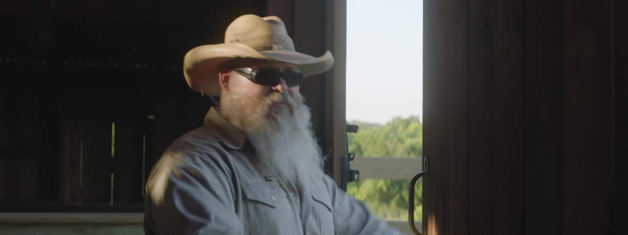 A man with a big white beard inside a barn opens up the doors