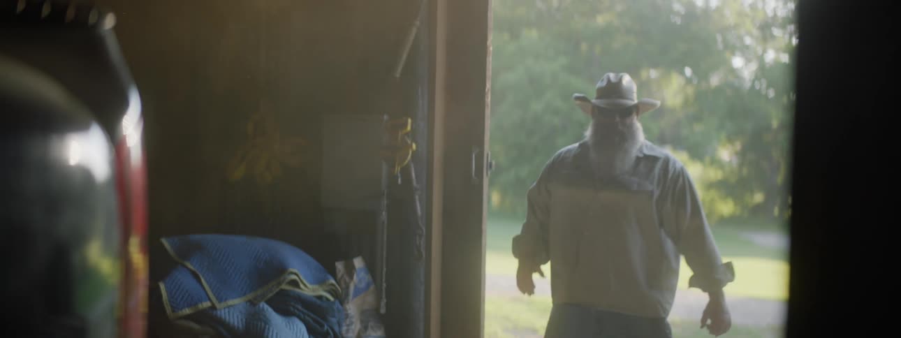 A cowboy slides open a barn door letting in the sunlight