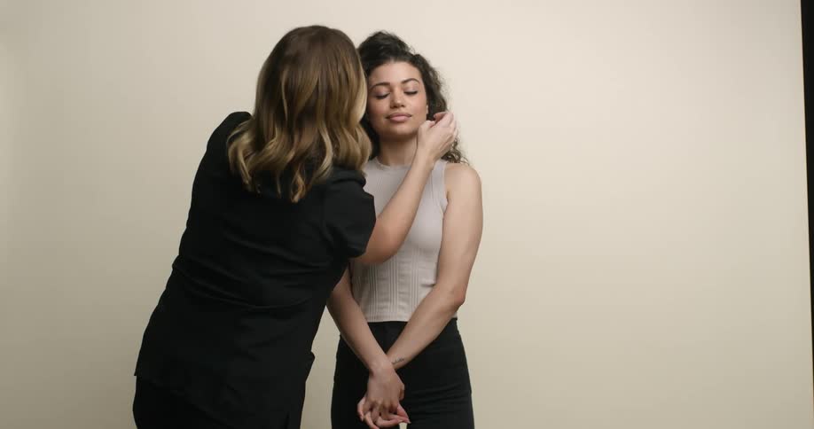 A young Polynesian woman having her dark, curly hair adjusted for a photo shoot by a female stylist.