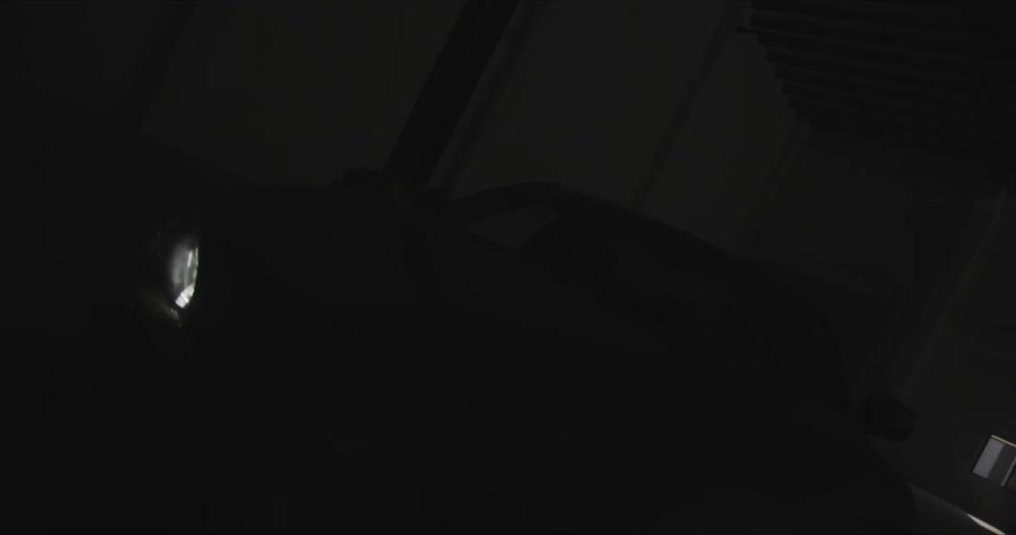 Car sits with its headlights on in dark garage with the door down and sunlight coming through small garage door windows