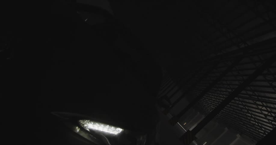 A car with headlights in a garage with pillars and a wall in the background