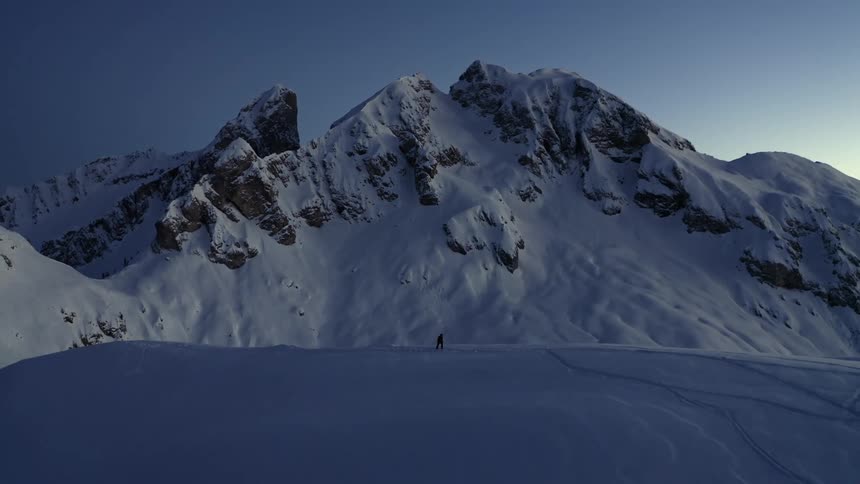 Aerial view of man hiking snowy mountain with a view of high snowy mountains in the background at dusk
