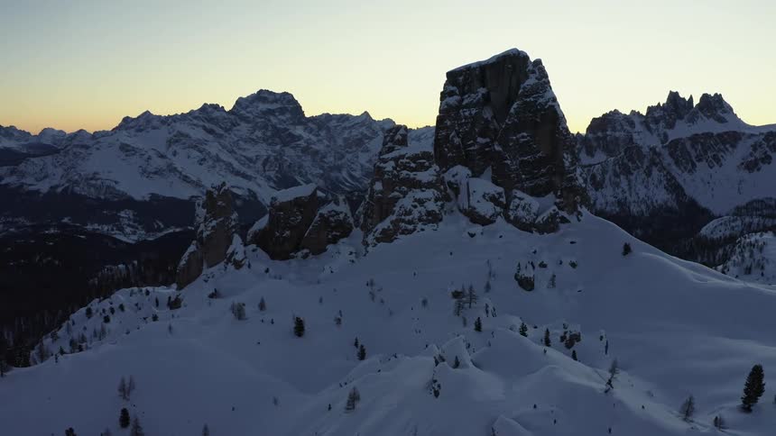 Aerial view of rock promontories covered with snow near a mountain range at sunset