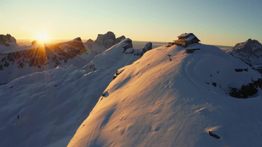 A mountain range with a house covered in snow and ice with the sky and clouds in the background