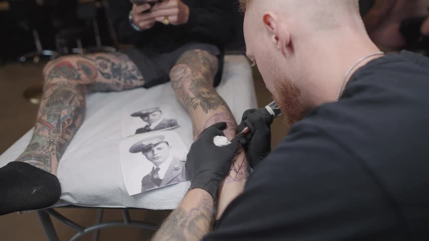 A man is drawing a tattoo on a persons leg