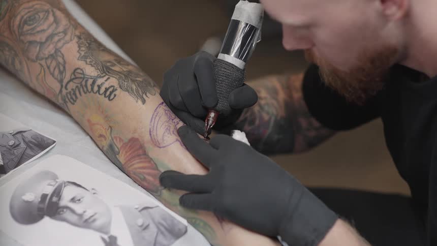 A tattoo artist is drawing a tattoo of a mans face on a persons leg