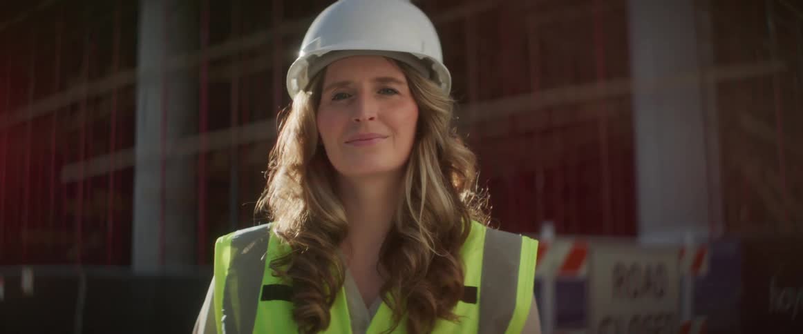 A woman in a hardhat poses by the construction site